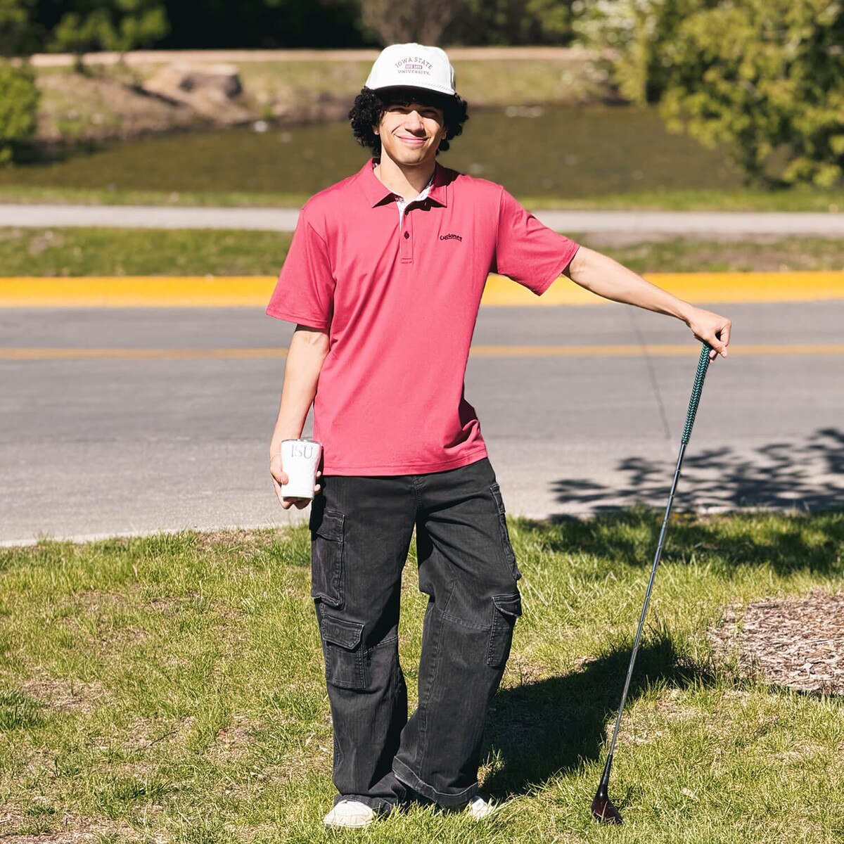 Student wearing Swannies Cyclones Script Cardinal James H Polo and posing with a golf club, hat, and golf cup.